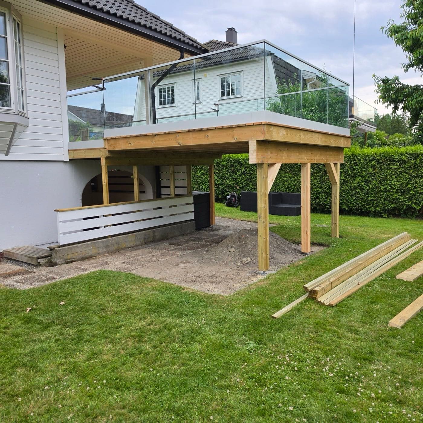 Terrassetilbygg under bygging med søyler og materialer på plen, Ås